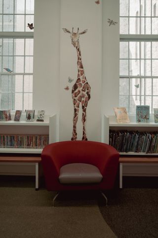 An armchair in a youth library with a drawing of a giraffe on the wall behind it