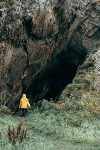 A small person in a yellow jacket facing a way bigger hole in a hill