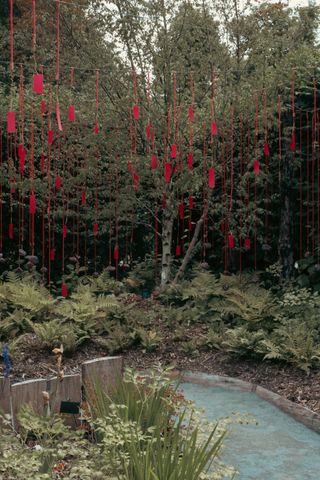 A garden decorated with a lot of red pieces of paper suspended by red strings.