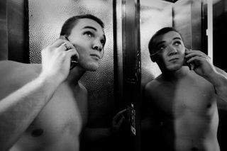 A nude man on the phone in an elevator with a mirror