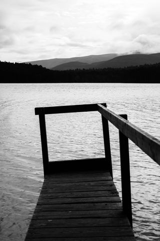 Black and white view of a skewed wooden pontoon on a lake with mountains in the background