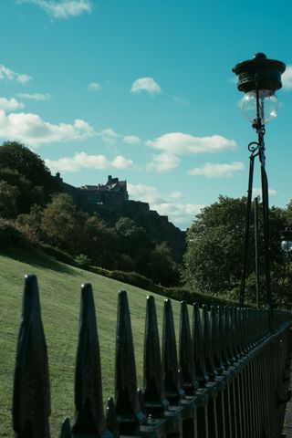 An old castle up a hill in the background and a fence with a street lamp in the foreground