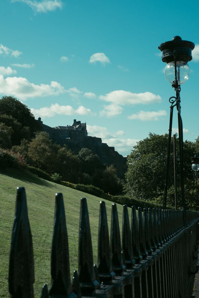 An old castle up a hill in the background and a fence with a street lamp in the foreground